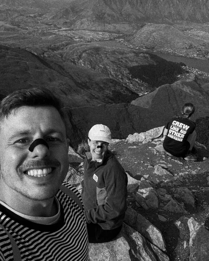 Three hikers on a mountain summit; one wears nasal tape for better breathing