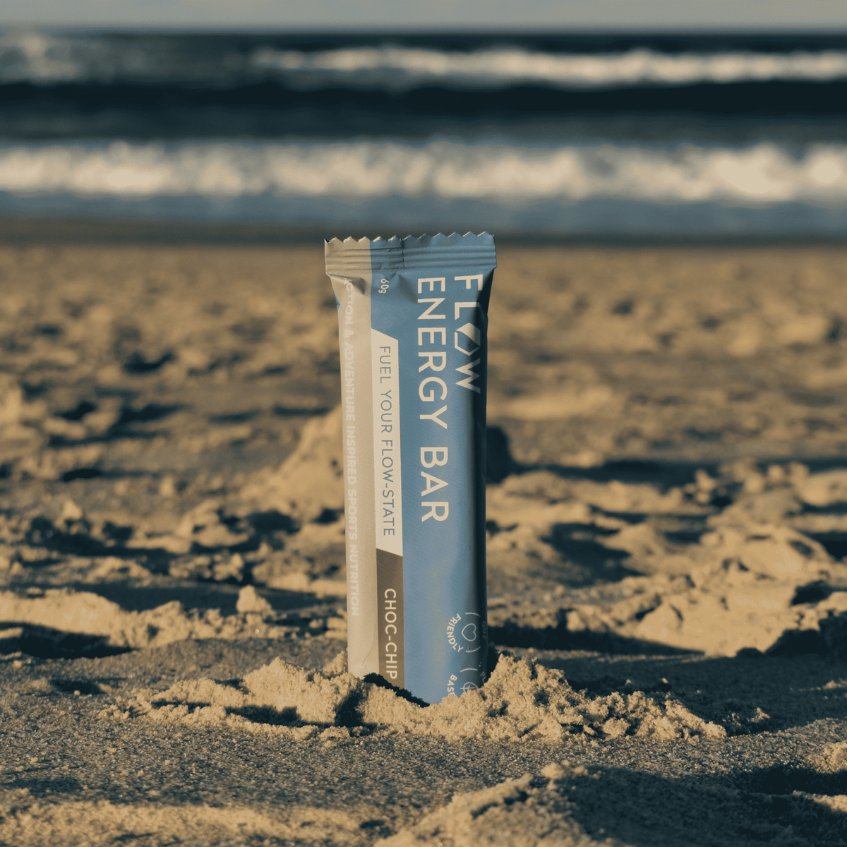 Flow Energy Bar packaging on a sandy beach with ocean waves in the background