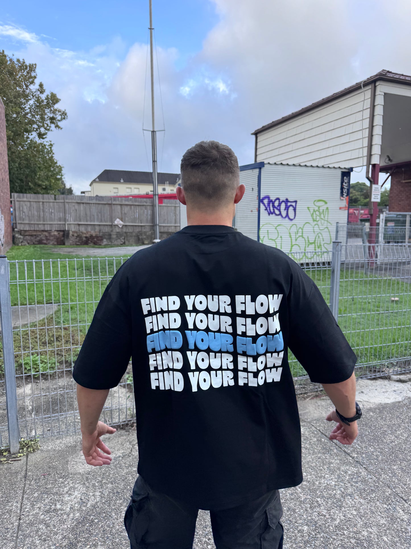 Person wearing a black t-shirt with 'Find Your Flow' text on the back, standing outdoors.