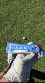 Flow Recovery Bar held by a gloved hand on grass with a golf ball in the background