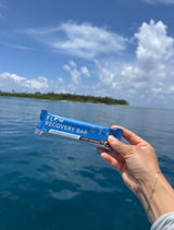 Hand holding a Flow Recovery Bar with a scenic background of water and sky.